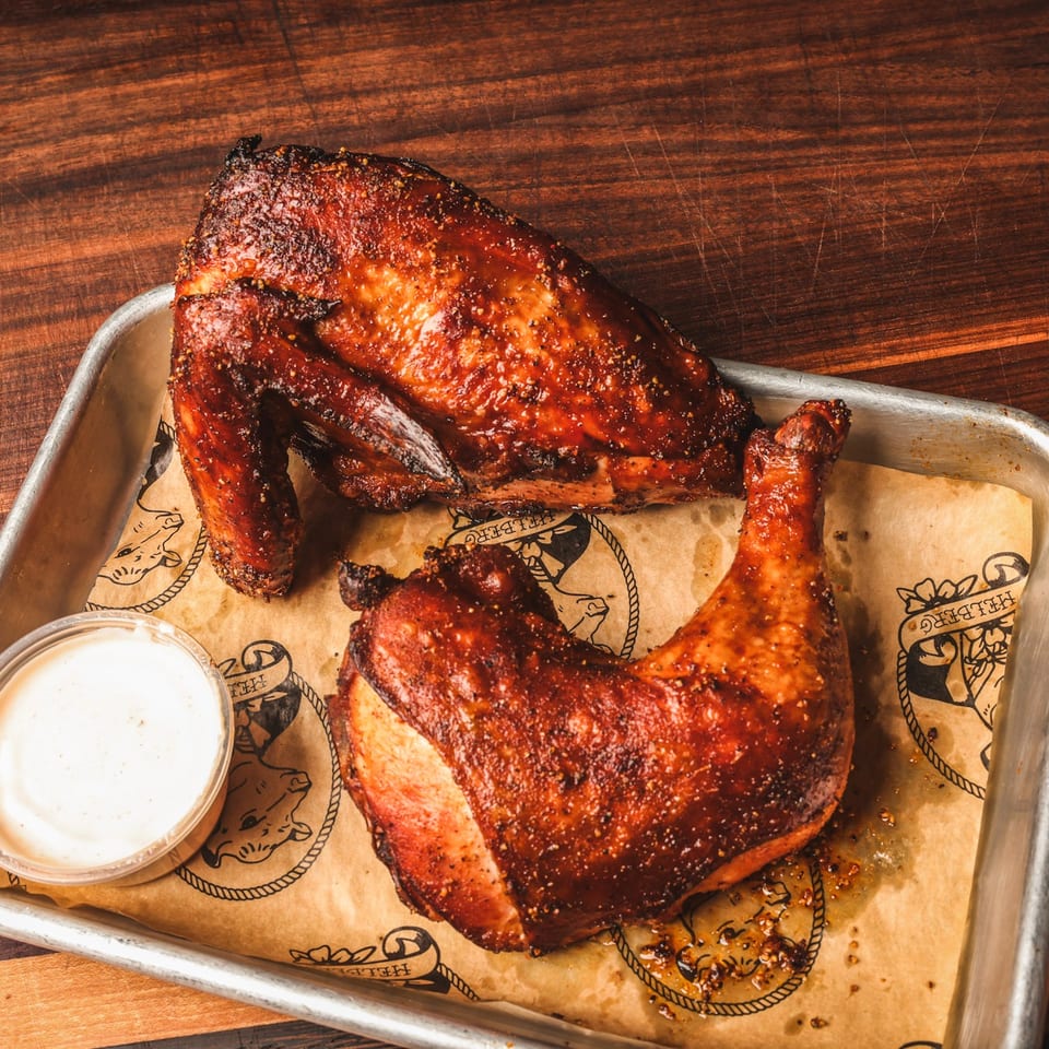 Smoky glazed barbecue chicken pieces served on a lined metal tray with dipping sauce atop a wooden table.